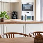 Kitchen with wooden countertop, white cabinets, and built-in oven. A basket with bread sits on the table.