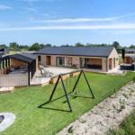 Modern wooden cabin with terrace, swing, fire pit, and sauna in the garden.