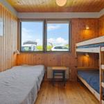 Room with double bed and bunk bed, wooden walls and window overlooking parking lot.