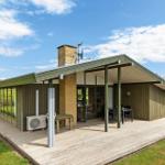 Modern cabin with terrace, garden, and field view under blue sky.