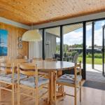 Dining area with wooden table and chairs, large window to garden, wall painting with sailboat.