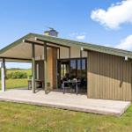 Modern wooden cabin with terrace, grill, and view of fields under blue sky.