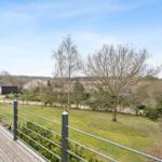 Holzterrasse mit Metallgeländer und Blick auf grünen Garten und Bäume.