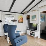 Wohnzimmer mit blauen Sesseln, Fernseher und weißen Wänden. Durchgang zu Schlafzimmer.
