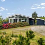 Moderne Villa mit großem Garten und blühenden Sträuchern. Garage und Anhänger sind vorhanden.