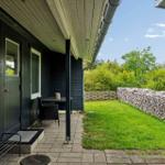 Terrasse mit Tisch und Stuhl neben grünem Garten und Holzstapel.