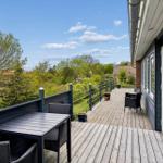Terrasse mit Tisch und Stühlen, Blick auf grüne Umgebung und Himmel.