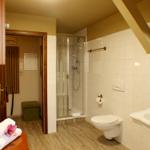 Badezimmer mit Dusche, Toilette und Waschbecken. Holzboden und weiße Fliesen.