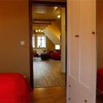 Zimmer mit rotem Bett und Blick in Wohnbereich mit Sofa und Holzboden.