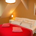Schlafzimmer mit Dachschrägen, weißem Bett und rotem Deckenbezug.