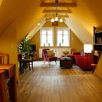 Wohn- und Essbereich mit Holzboden, rotem Sofa und Holztisch. Dachschräge mit Fenstern.