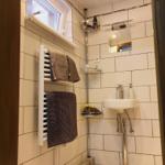 Badezimmer mit Dusche, Waschbecken und Heizkörper. Weiße Fliesen und Holzboden.