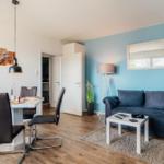 Wohn- und Essbereich mit Sofa, Tisch und Stühlen. Blaue Wand, Spiegel und Pflanze.