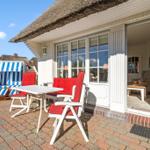 Terrasse mit Tisch, Stühlen und Strandkorb vor einem Haus mit Strohdach.