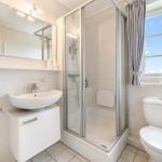 Badezimmer mit Dusche, Waschbecken und Toilette. Fenster mit Blick auf Himmel.