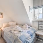 Schlafzimmer mit Dachschrägen, Bett mit Handtüchern, Fenster mit Vorhängen und Stuhl.