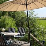 Terrasse mit Tisch, Stühlen und Sonnenschirm. Blick auf grüne Wiesen und Bäume.