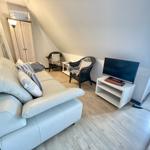 Wohnzimmer mit Sofa, zwei Stühlen, Fernseher und Kleiderschrank unter Dachschrägen.