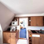 Kitchen with wooden cabinets, sink, and microwave. Passage to a room with blue carpet.