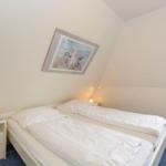 Bedroom with double bed, nightstand, and picture on the wall. Window with blue curtains.