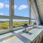 Großes Fenster mit Blick auf Grasland und Meer. Holzverkleidung und Fensterbank mit Lüftungsschlitzen.