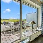 Terrasse mit Tisch und Stühlen, Blick auf Grünland und Meer.