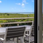 Terrasse mit Tisch und Stühlen, Blick auf grüne Wiesen und Meer.