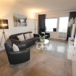 Living room with sofa, chairs, and glass table. Terrace with view. White furnishings.