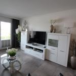 Living room with TV, glass table, and white cabinets. Doorway and balcony door visible.