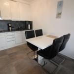 Kitchen with dining area, white countertop, black chairs, and wall clock.