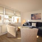 Wohnzimmer mit Sofa, zwei Sesseln und Fenstern mit Jalousien.
