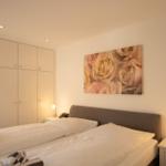 Schlafzimmer mit Doppelbett, Kleiderschrank und Blumenbild an der Wand.