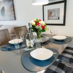 Dining table set for four with vase and bottle on the tabletop.