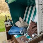 Green beach chair with cushions, blanket, and glasses. Background: grass and stone path.