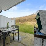 Terrace with table, chairs, and beach chair. Background: grassy area and hedge.