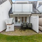 Backyard with table, chairs, wicker furniture, and garden gate. White wall and stone paving.
