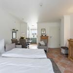 Bedroom with double bed, living area, and kitchen in the background.