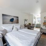 Bedroom with double bed, armchairs, and wall art. Kitchen and dining area are visible.