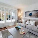 Living room with sofa, coffee table, and large windows. Wall art shows a blue boat.