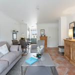 Living room with sofa, coffee table, and TV. Terracotta floor and wooden furniture.