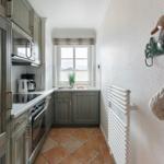 Kitchen with gray cabinets, stove, and window. Oven mitts and a duck hang on the wall.