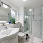 Bathroom with shower, sink, and toilet. White tiles and towels.