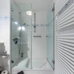Shower with glass enclosure, white tiles, and heater.