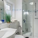 Bathroom with shower, sink, and toilet. White tiles and plant visible.