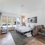 Living room with sofa bed, dining table and TV. Large window front with view outside.