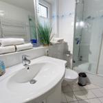 Bathroom with shower, sink, and toilet. White tiles and towels.