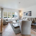 Living room with sofa, armchairs, dining table, and TV. Large window front with outdoor view.