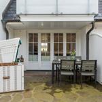 Terrace with table, chairs, and white beach chair. Background: white house wall and glass doors.