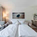 Bedroom with bed, armchair, and wall art. Adjacent dining area with table and chairs.