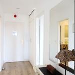 Flur mit Spiegel, Lampe und Tür. Holzfußboden und weiße Wände.